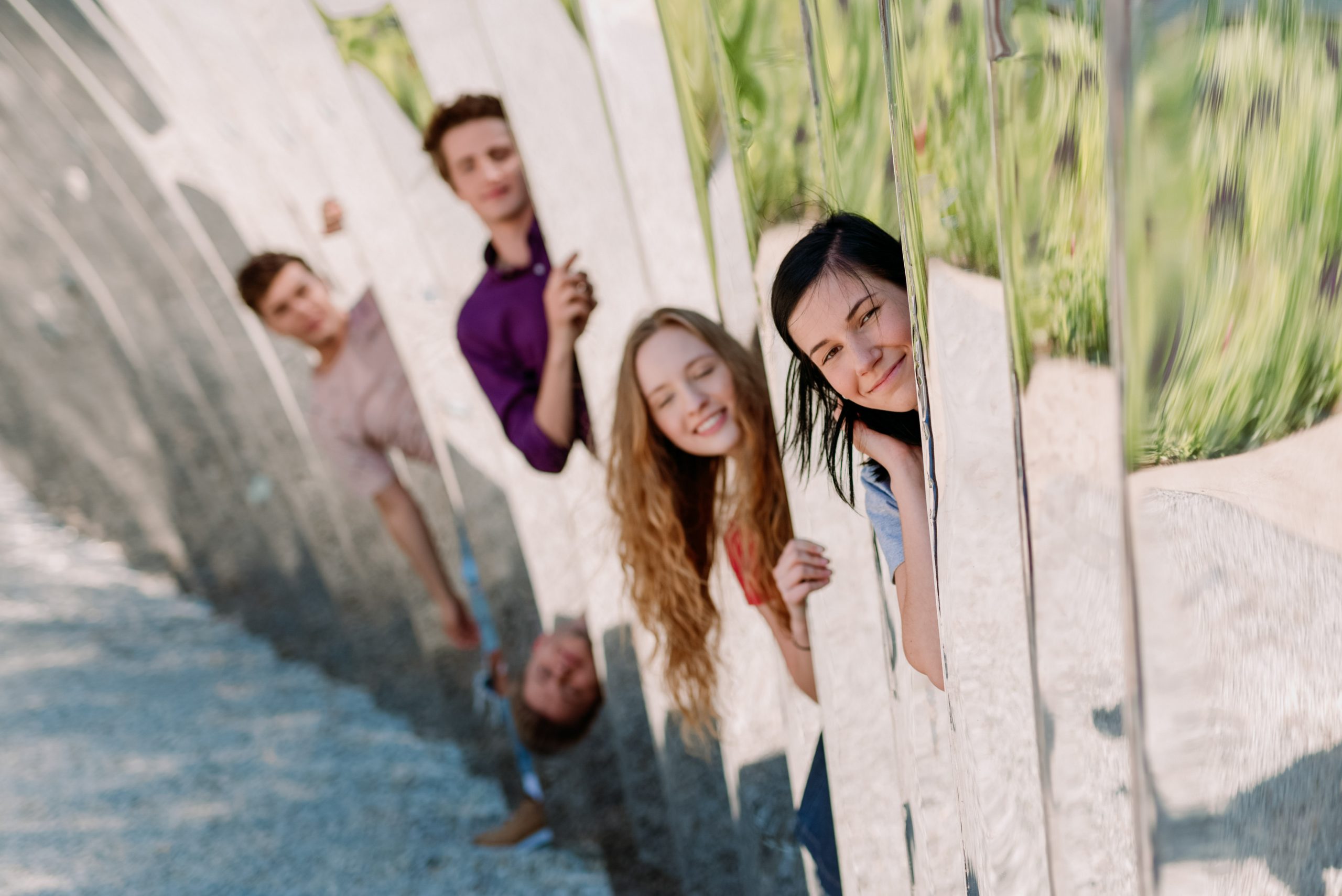 Czwórka młodych osób; dwie dziewczyny i dwóch chłopaków wygląda głowami z pomiędzy ściany luster ustawionych jeden za drugim.