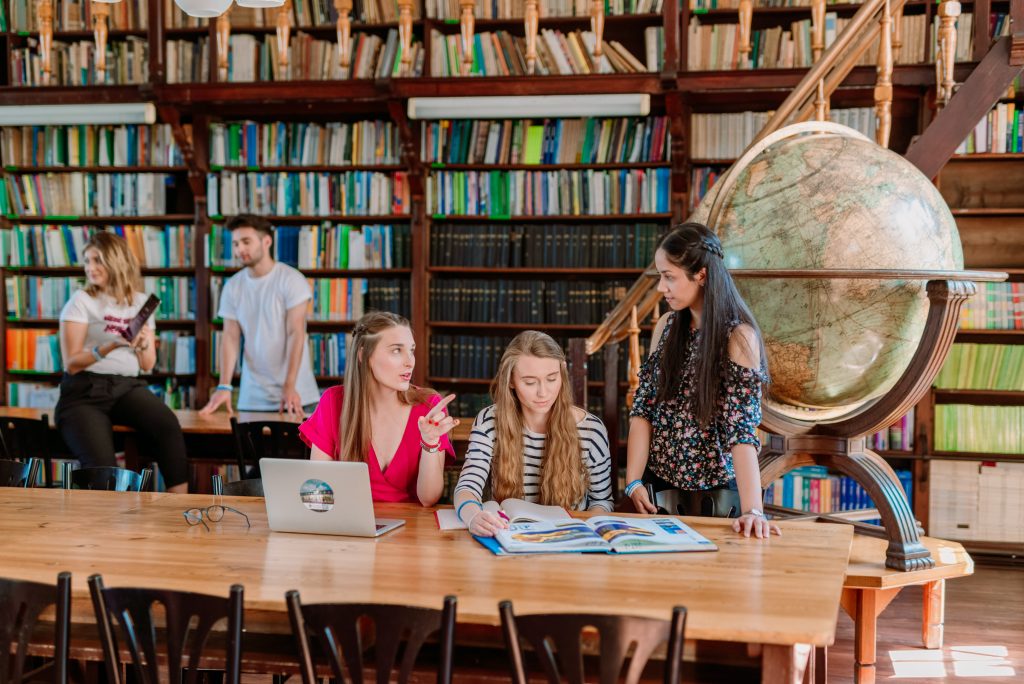 studenci rozmawiają ze sobą siedząc przy stole w bibliotece