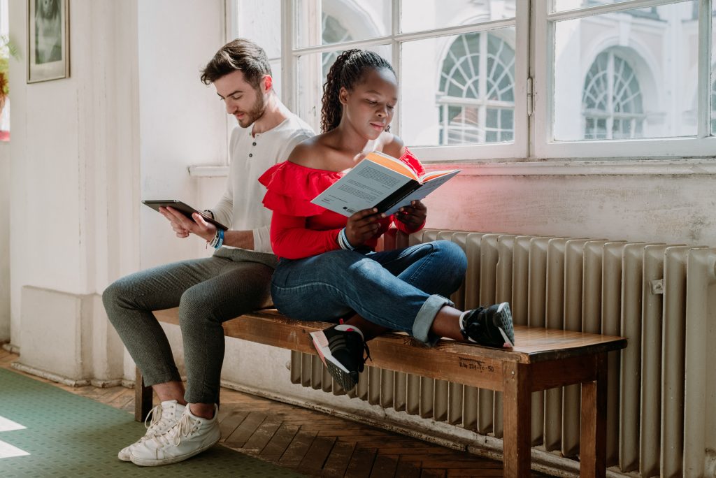 Chłopak i dziewczyna siedzą na ławce w budynku uczelni i czytają książki.