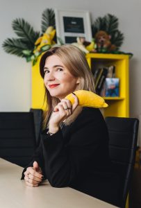 Uśmiechnięta kobieta z pluszowym bananem w ręku siedzi przy biurku