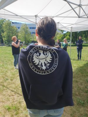Dziewczyna stojąca tyłem, z bluzą z logo uniwersytetu wrocławskiego, narzuconą na ramiona..
