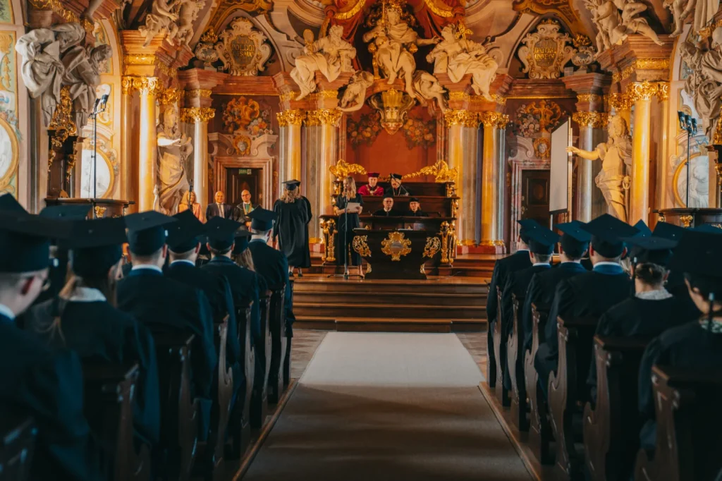 Absolwenci siedzą w ławach w Auli Leopoldina podczas wręczenia dyplomów ukończenia studiów