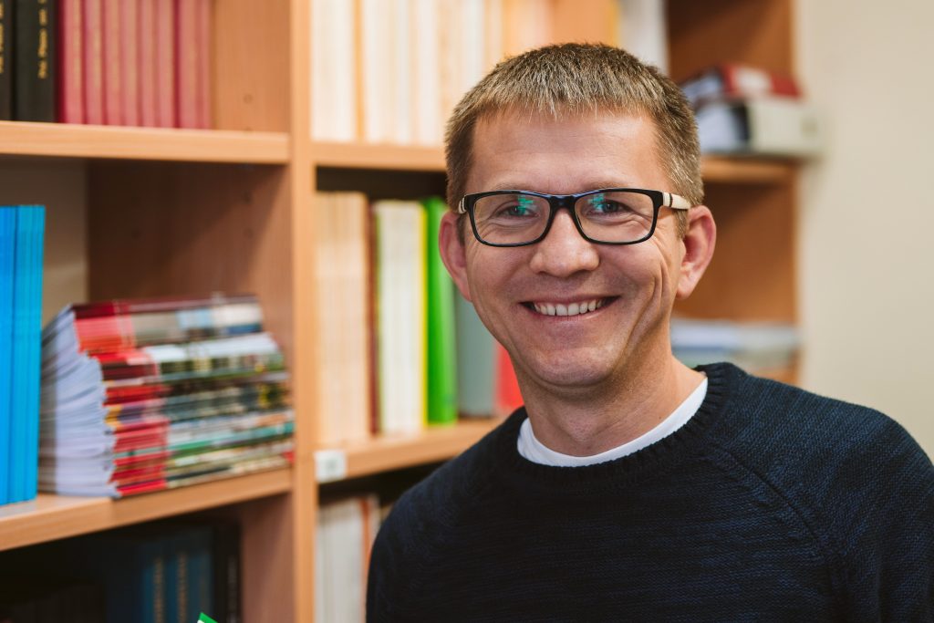 Portret przedstawiający uśmiechniętego mężczyznę w czarnym swetrze