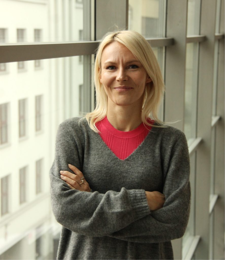 uśmiechnięta kobieta stojąca przy oknie z założonymi rękami