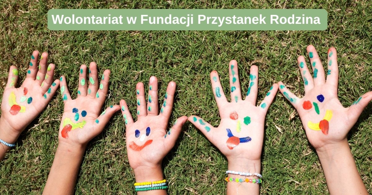 dziecięce dłonie na trawie z narysowanymi na nich kolorowymi uśmiechami a na górze napis: wolontariat w fundacji przystanek rodzina